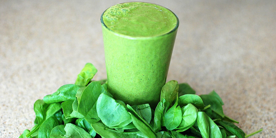 green smoothie in a glass surrounded by green leaves