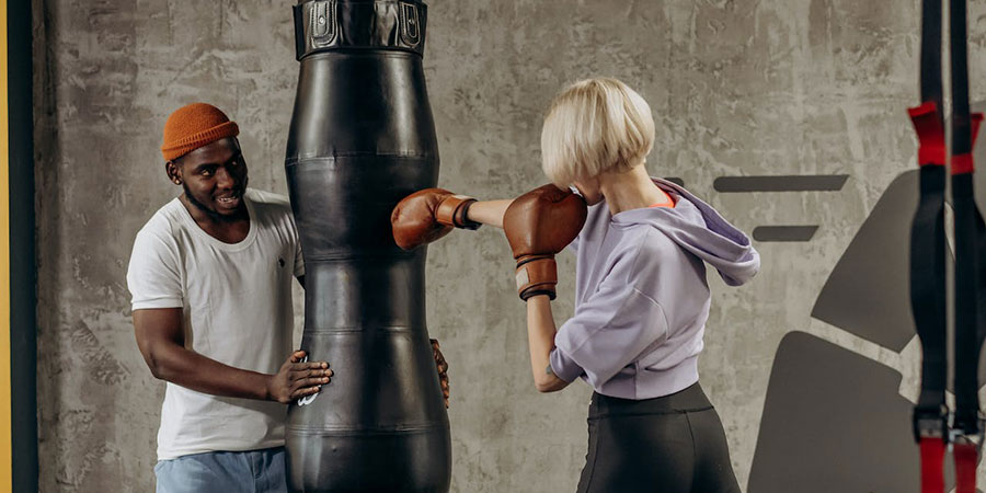 woman with short blonde hair training with a punching bag while a black man holding it